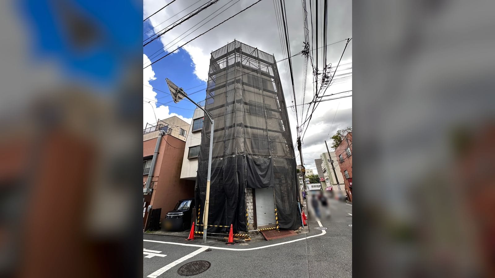 足場とメッシュシートで全体を覆われた建物。1階はシャッターが下り、周囲にコーンが置かれている